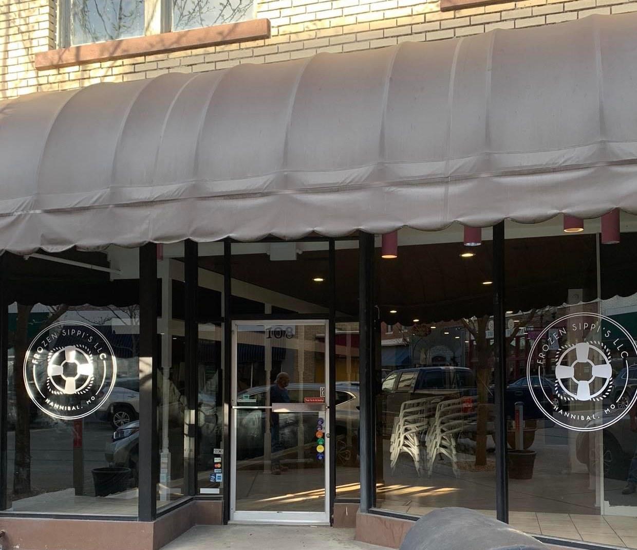 The Frozen Sippi’s shopfront on North Main Street: a fabric awning over two plate glass windows, each carrying the life ring roundel, and the glass door